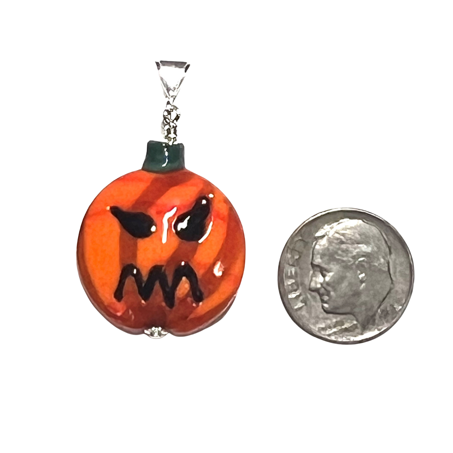 Pumpkin-shaped pendant with a face design next to a dime for scale on a white background