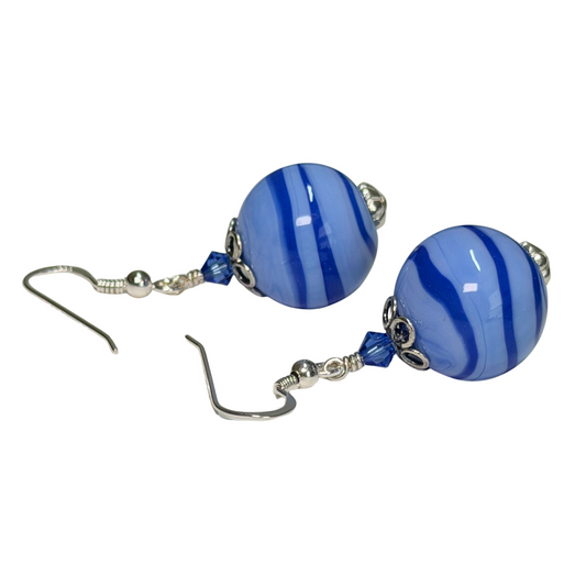A pair of drop earrings featuring round, glossy blue and white striped glass beads, suspended from silver-tone fishhook wires with small blue beads and silver spacer details, set against a plain white background.