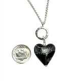 a dark gray heart shaped pendant next to a dime