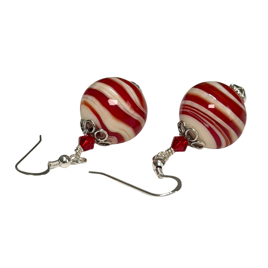 A pair of drop earrings featuring round, glossy red and white striped glass beads with silver-toned metal hooks and small red faceted beads, shown on a plain white background.