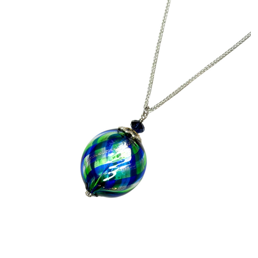 A glass pendant necklace featuring a round, hand-blown glass bead with a swirled pattern of green, blue,  suspended from a silver chain on a plain white background.