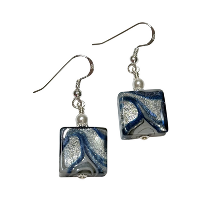 A pair of handmade square glass drop earrings featuring a marbled swirl pattern of blue, silver, and white, suspended from silver fishhook wires with small white pearl beads.