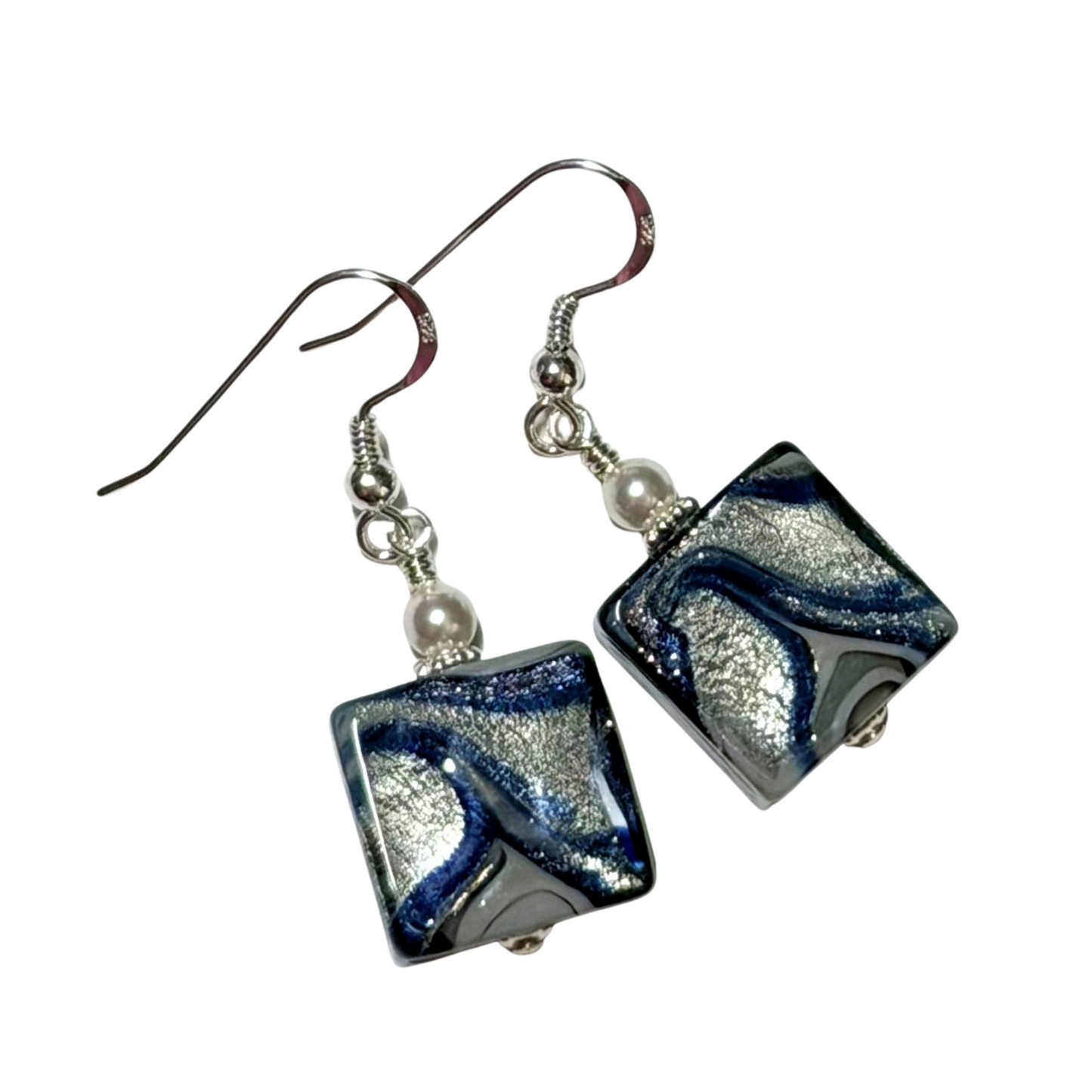 A pair of handmade square glass drop earrings featuring a marbled swirl of dark blue, silver, and black, suspended from silver fishhook wires with small white pearl beads.