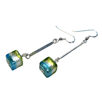 A pair of drop earrings featuring cube glass beads with a blue and green  pattern, suspended from sterling silver metal bars and fishhook wires, shown against a plain white background.