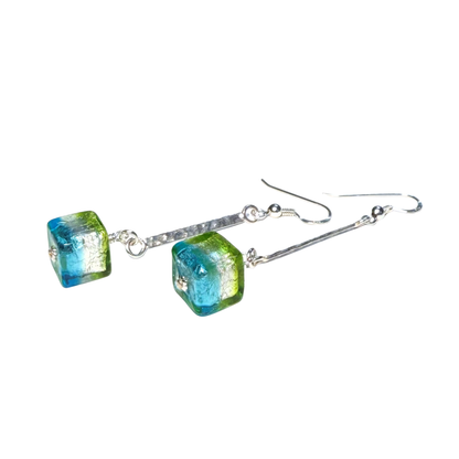 A pair of handmade drop earrings featuring square glass beads with a vibrant blue and green marbled pattern, suspended from textured silver wire hooks on a plain white background.