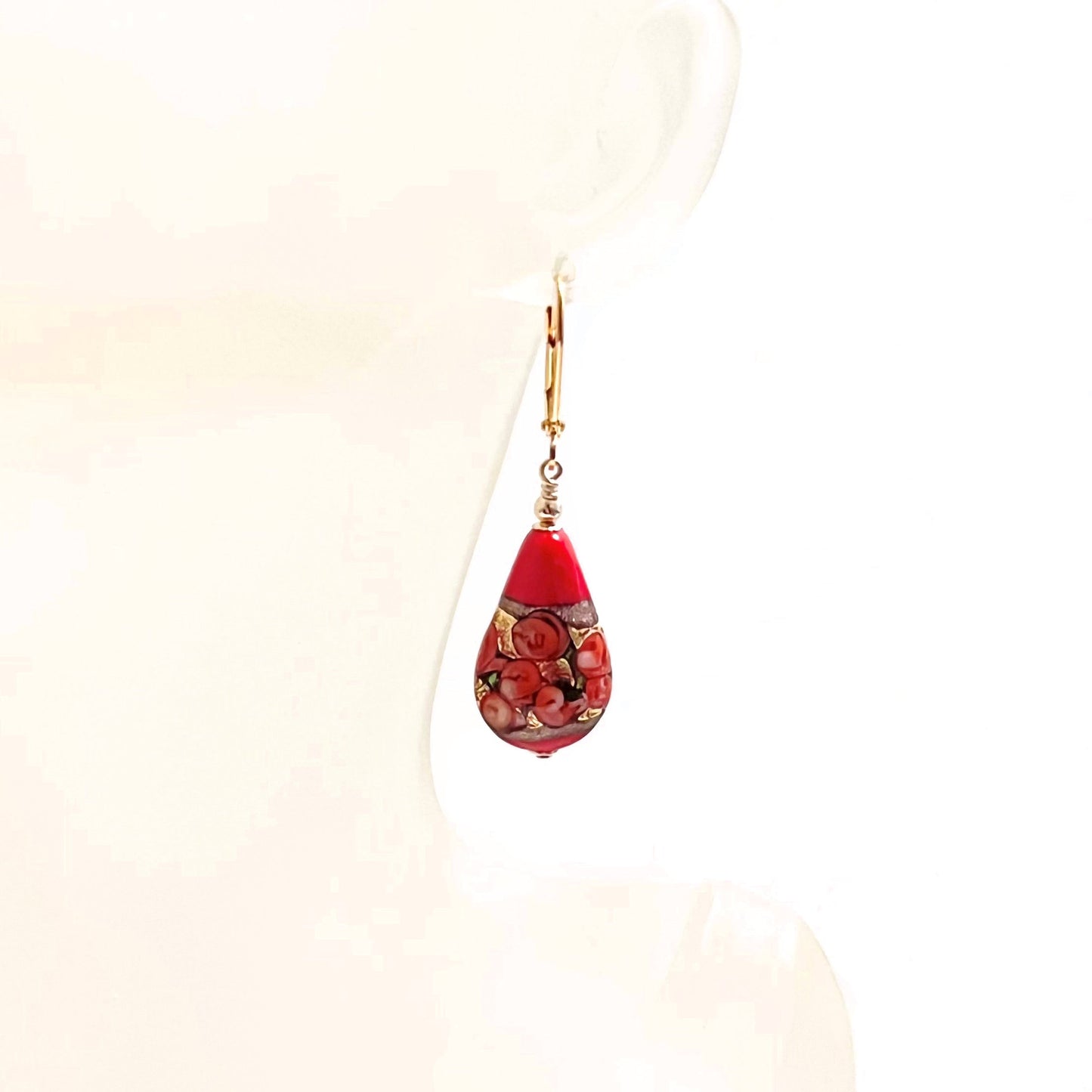 a pair of red and gold earrings hanging from a mannequin head