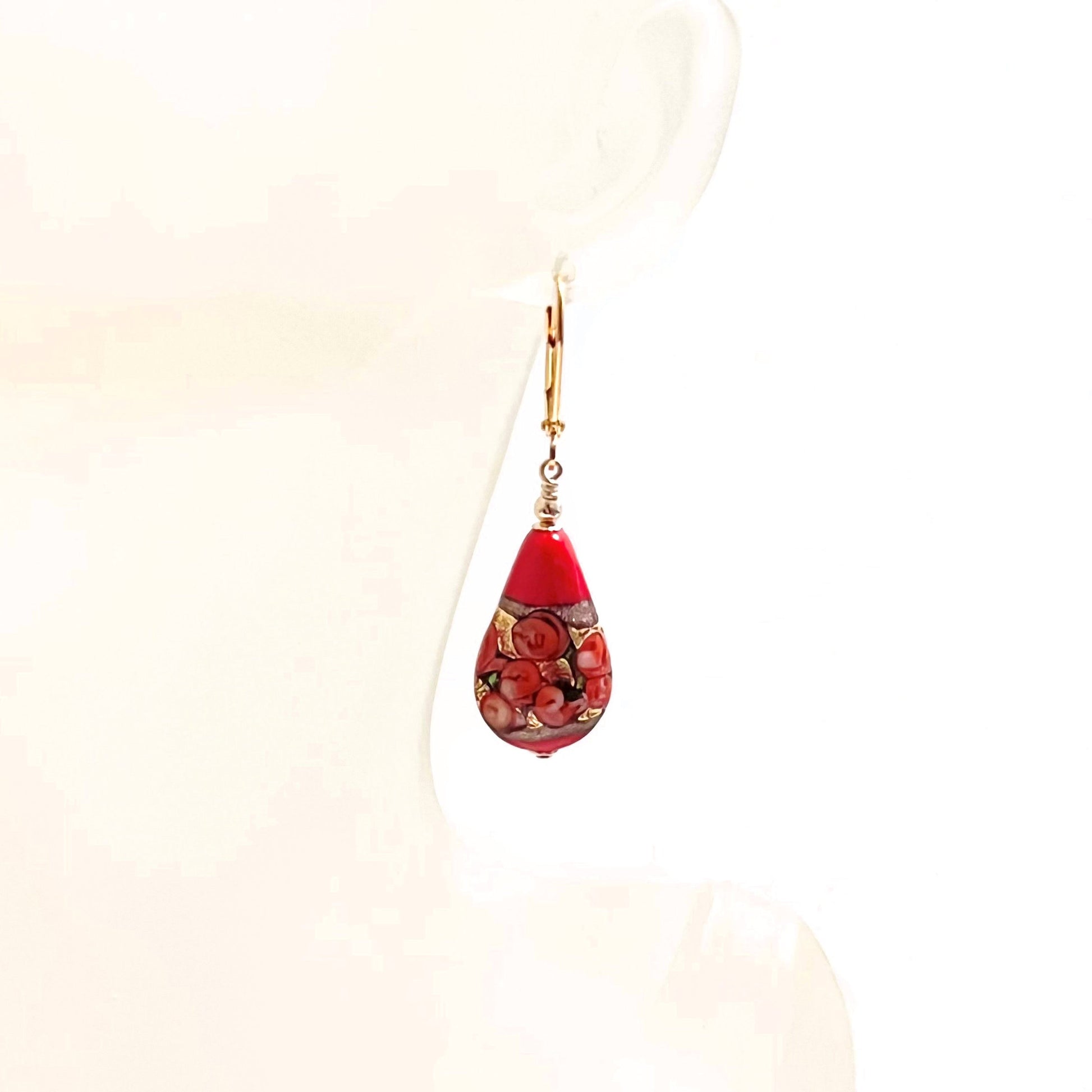 a pair of red and gold earrings hanging from a mannequin head